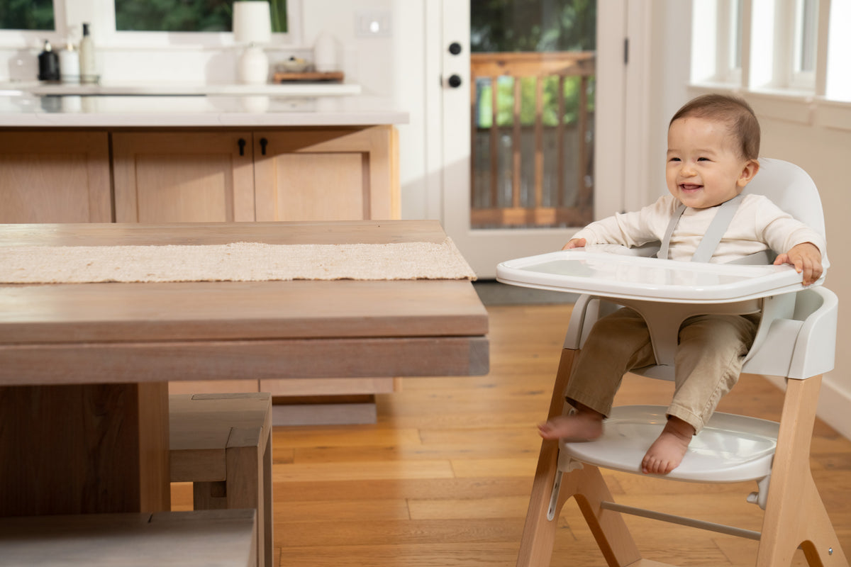 a child sits in the mockingbird high chair at the end of a long wooden table