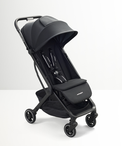 The Mockingbird Travel Stroller by Mockingbird, featuring a compact black design with a sunshade canopy, adjustable seat, safety harness, and four small wheels, is displayed on a white surface.