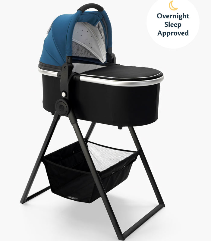 A modern baby bassinet with a blue canopy on a mockingbird-prod bassinet stand, featuring a storage basket underneath and labeled as "overnight sleep approved. #color_sea