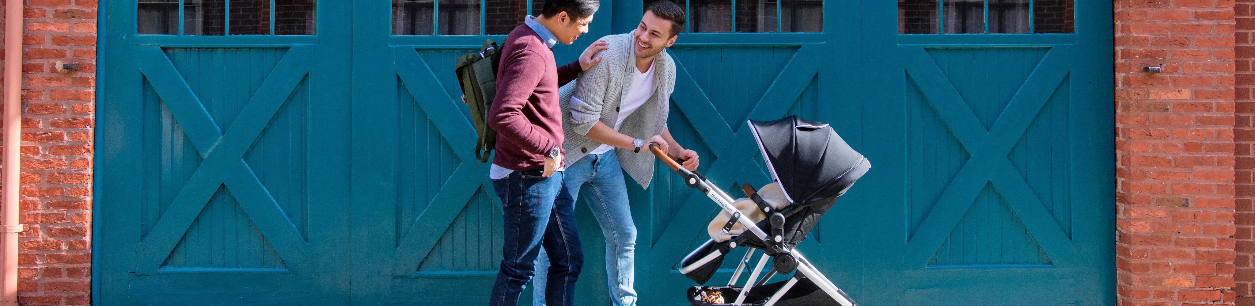 Two people talking while one pushes a stroller in front of large turquoise doors.