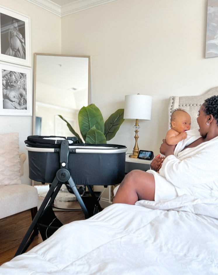 mom taking her infant out of the mockingbird bassinet and holding her infant beside it