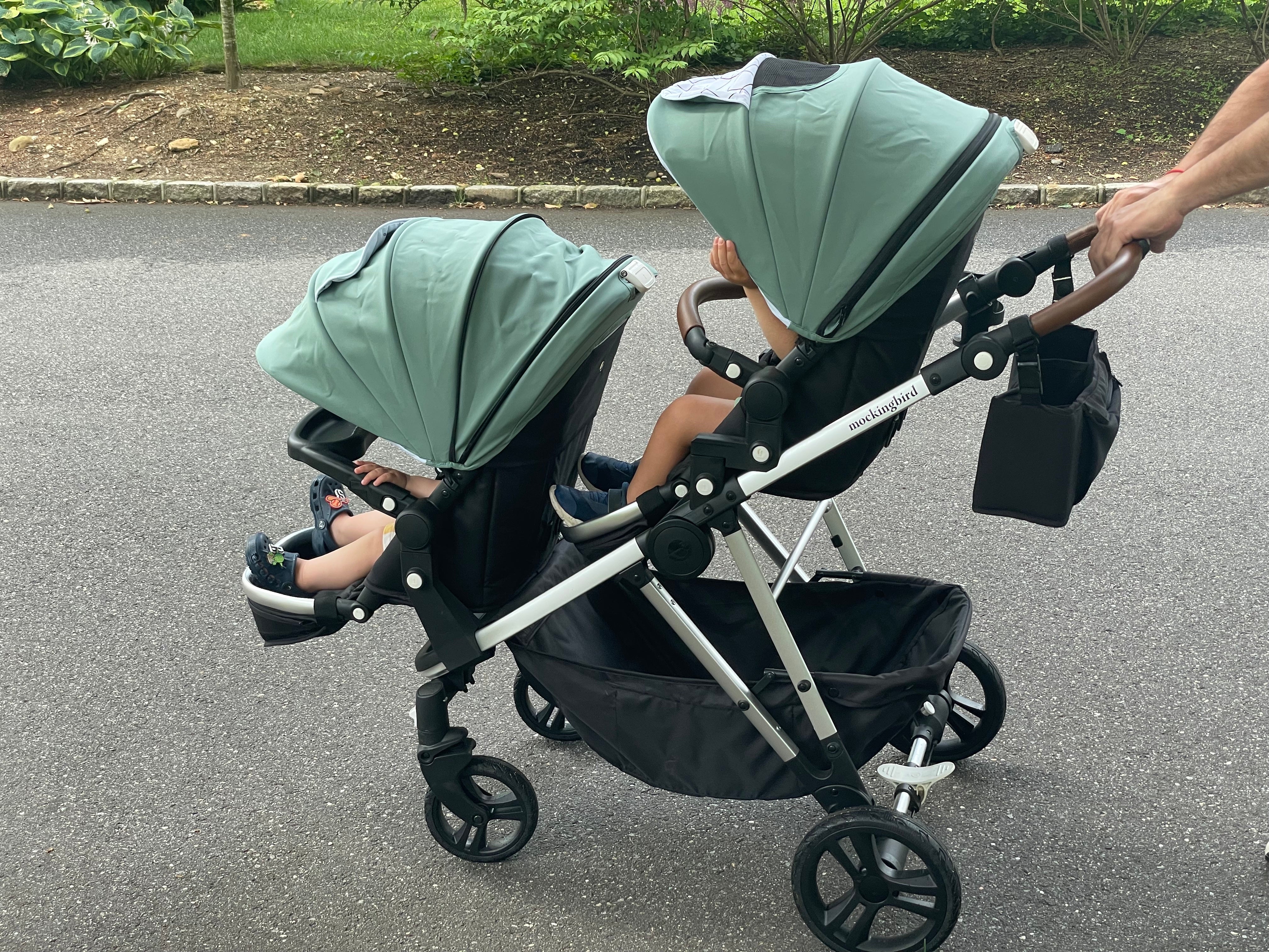 A man is holding a stroller with two children in it.