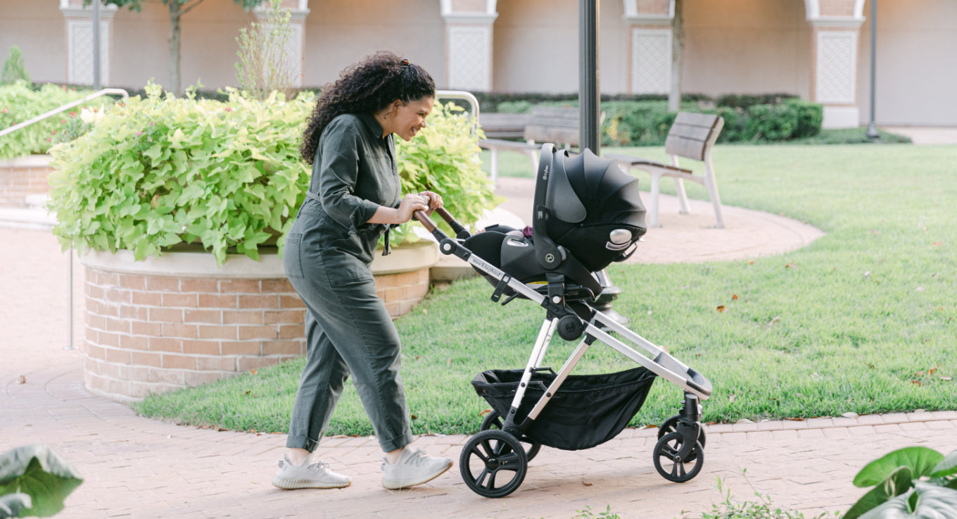 Woman pushing a baby stroller in a park-like setting.