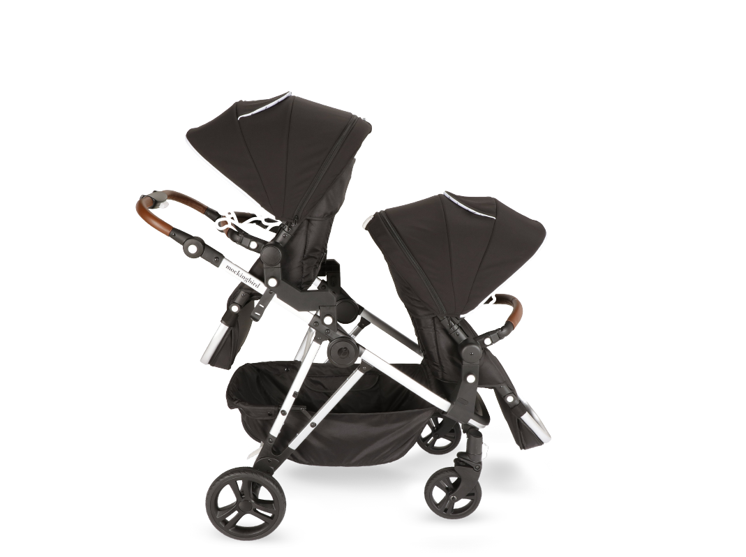 Double baby stroller with black canopies and a silver frame, isolated on a white background.