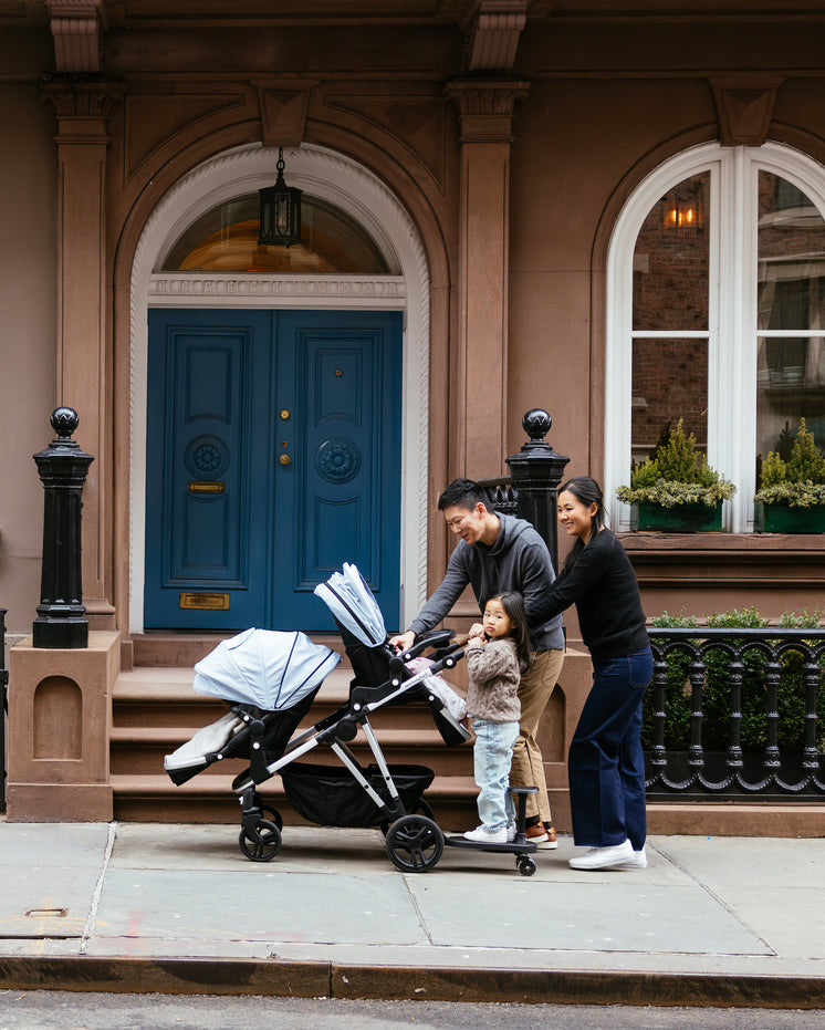 A family with a toddler and a baby in a stroller walking past a brownstone with a blue door.