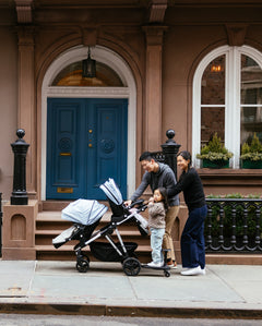 A family with a toddler and a baby in a stroller walking past a brownstone with a blue door.