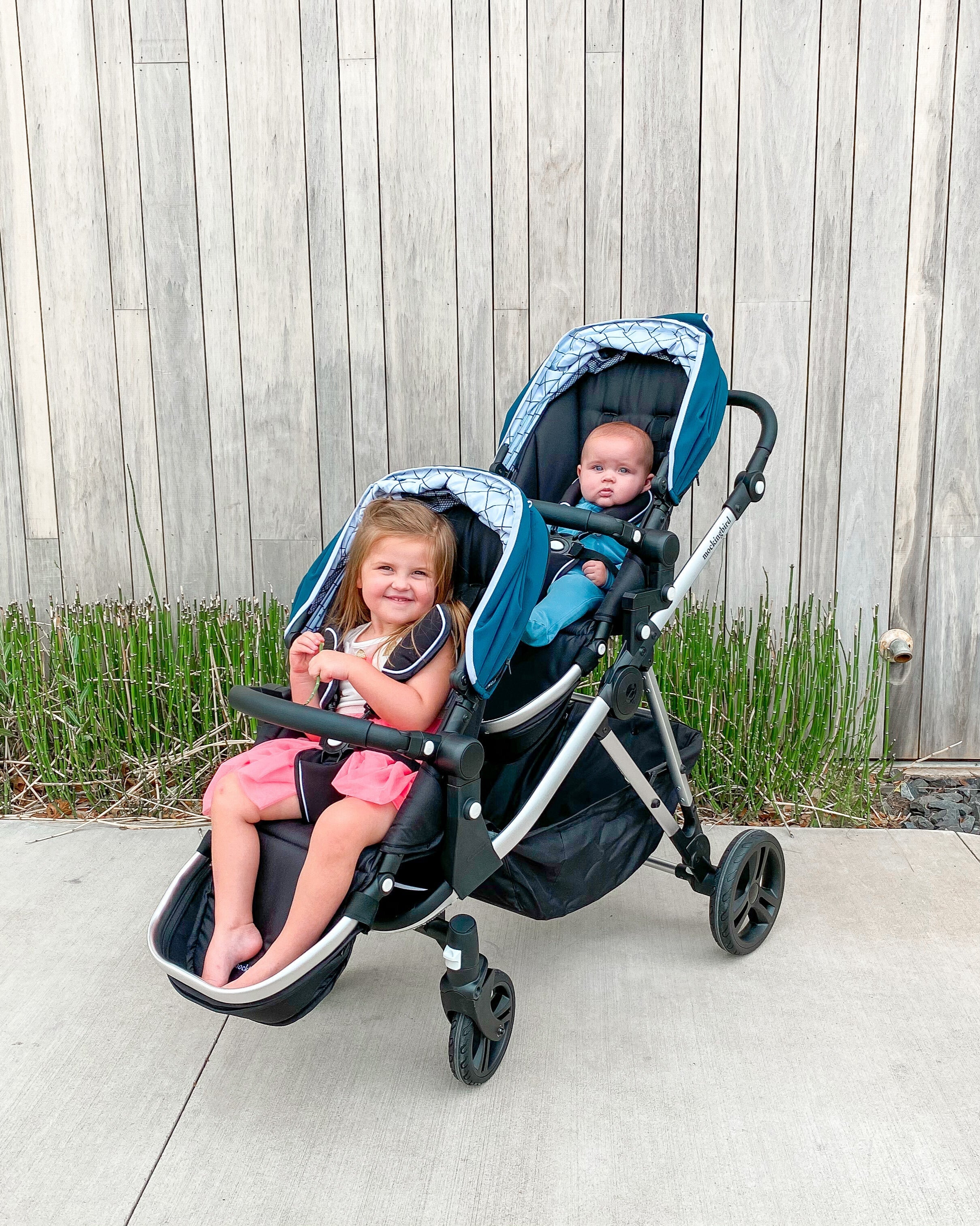 two kids in Mockingbird single to double stroller outside in front of fence