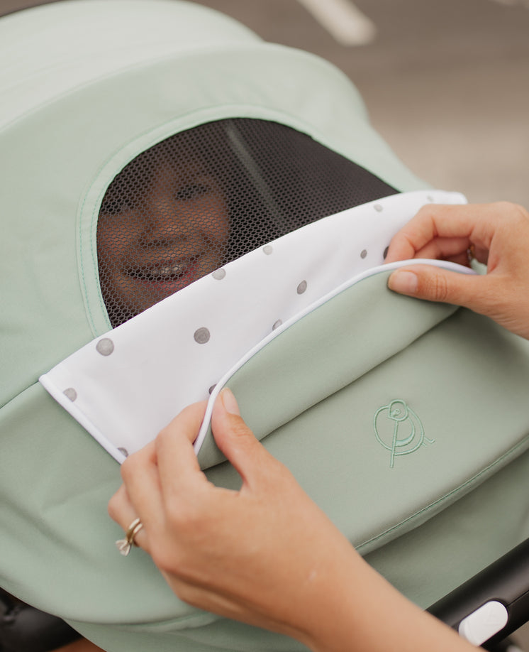 Hands adjusting the cover on a baby stroller with a glimpse of a smiling baby visible through the mesh window.