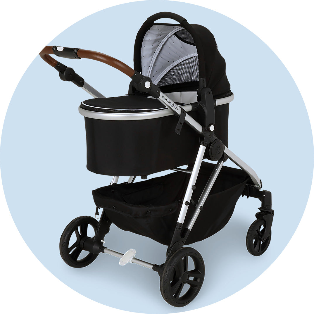 Modern black baby stroller with a silver frame on a light blue background.
