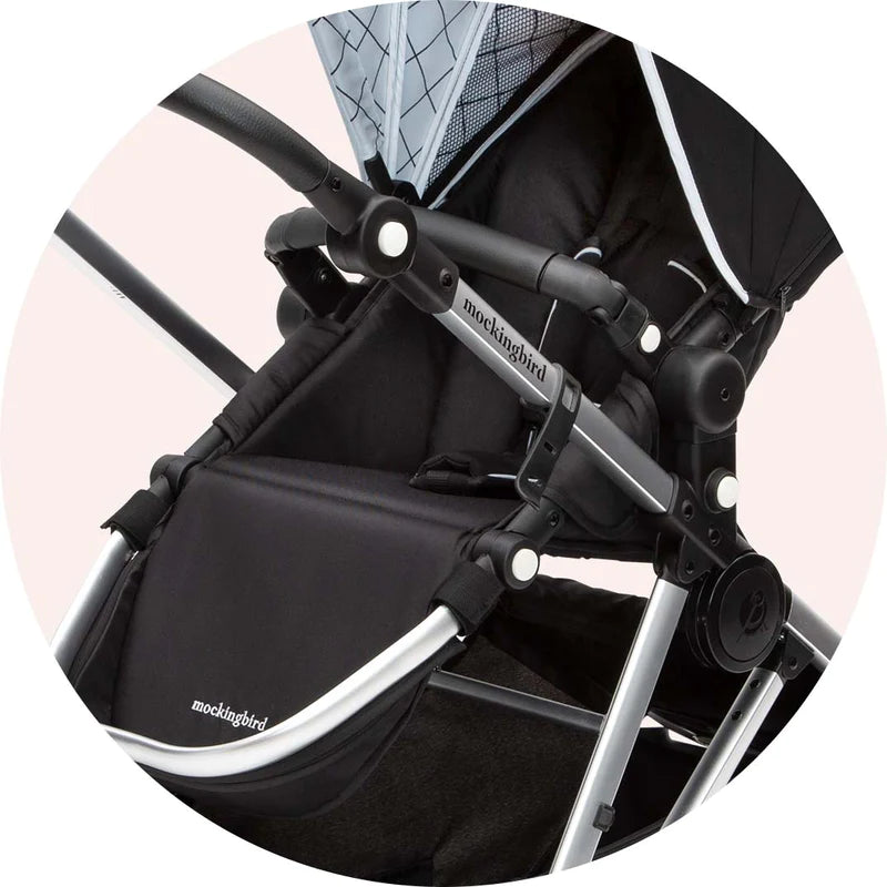 Close-up of a black and gray mockingbird stroller, focusing on its frame and fabric details against a pink background.