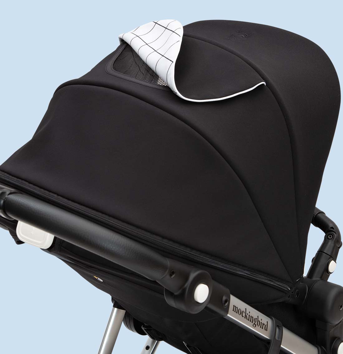 Black modern stroller with white-checked baby blanket draped over the canopy, set against a plain light blue background.