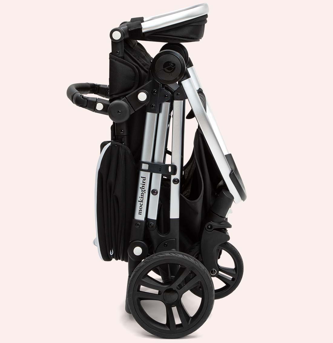 A black and silver folded baby stroller with large wheels against a pink background.
