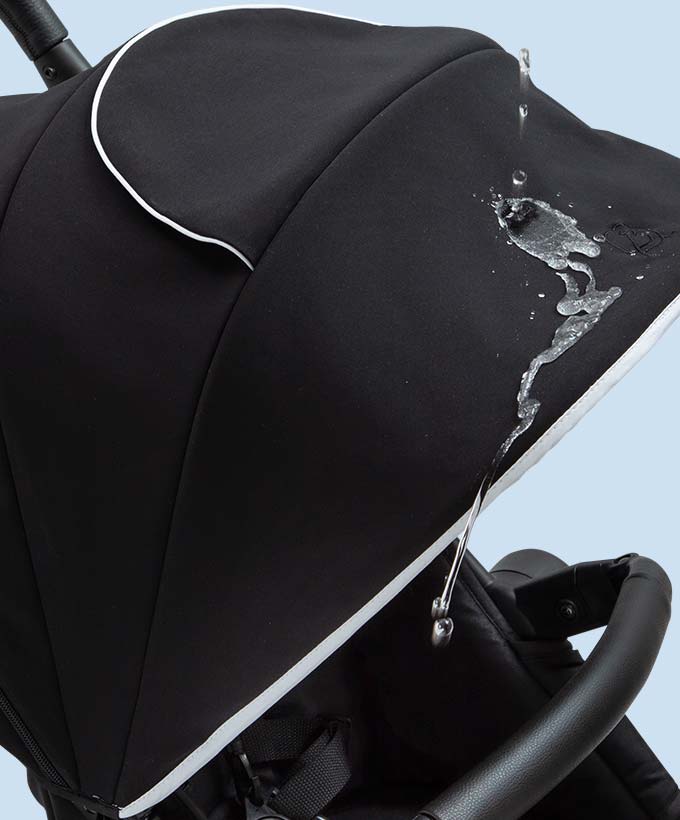 Close-up of water splashing on the black fabric canopy of a stroller, demonstrating water resistance.