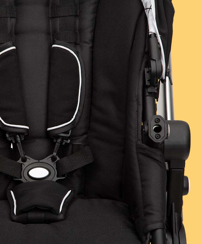 Close-up of an empty black baby stroller seat with visible harness and buckle against a yellow background.