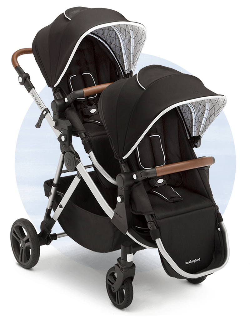 Double baby stroller with black canopies and brown handles, positioned against a white background.