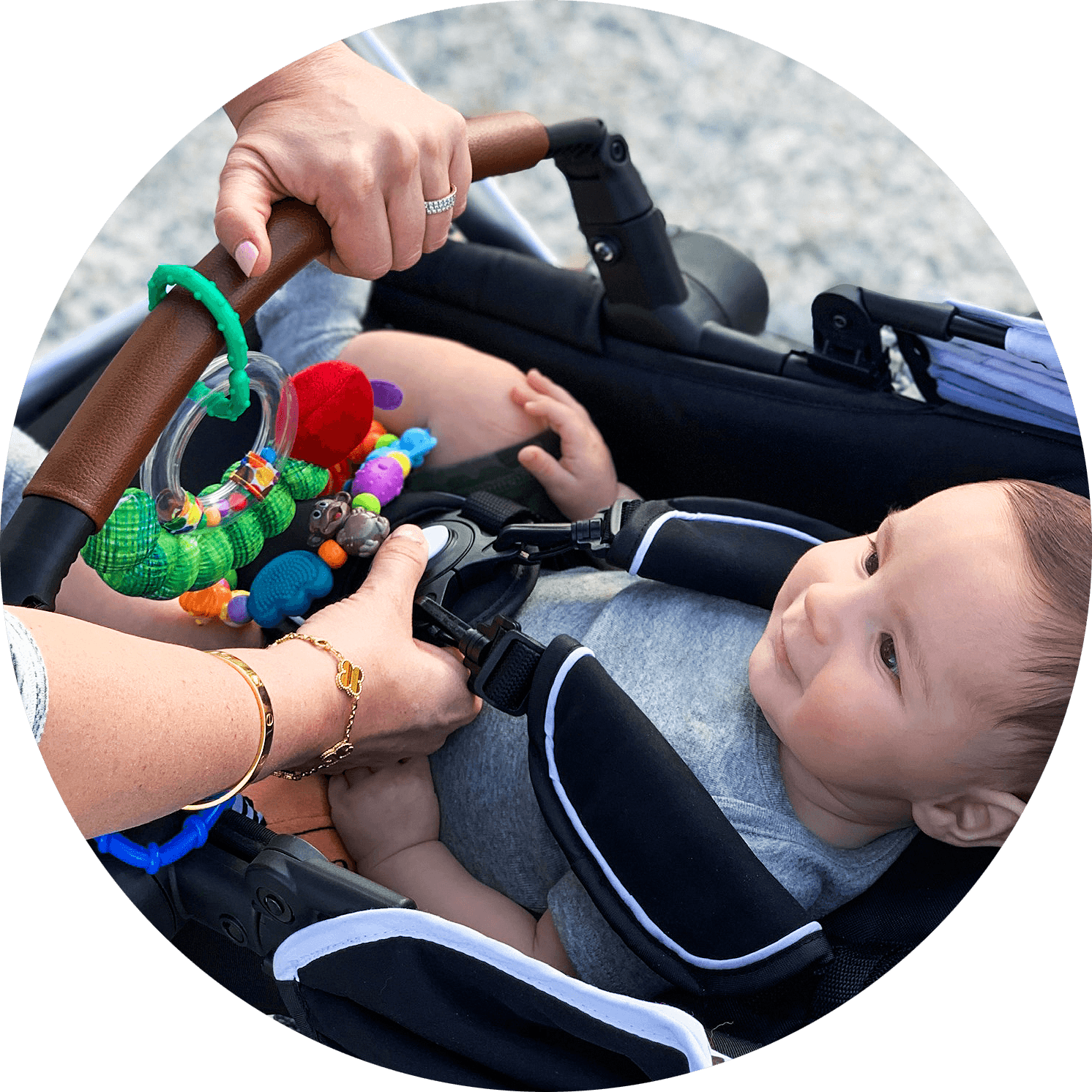 A baby in a stroller looks at a colorful toy held by an adult's hand, focusing on baby's curious expression.