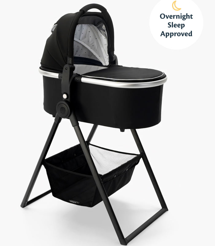Black mockingbird-prod baby bassinet with a hood on a metal bassinet stand, featuring a storage basket underneath and labeled "overnight sleep approved". #color_black