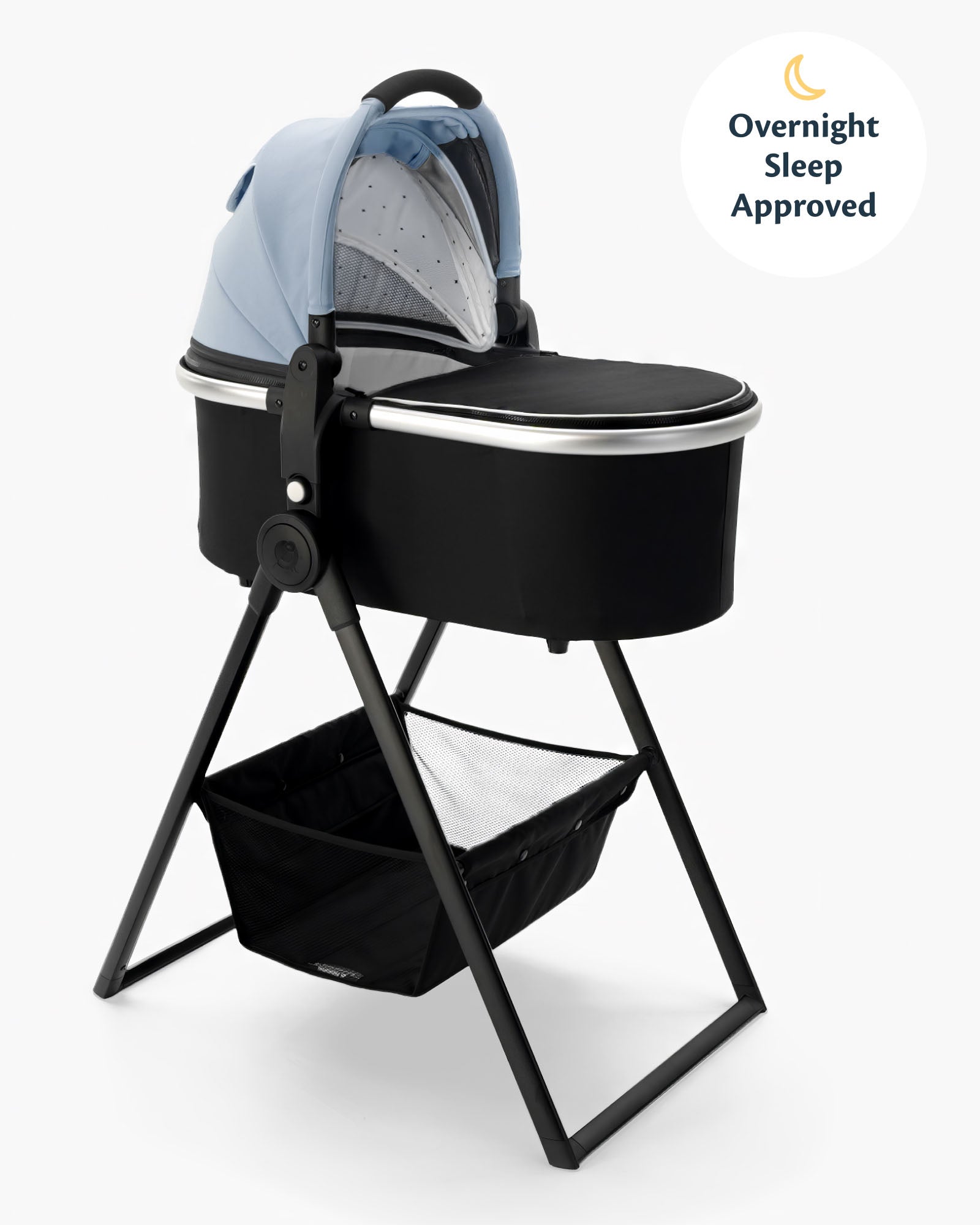 A mockingbird-prod bassinet with a blue canopy on a black bassinet stand, featuring a storage basket underneath and a label indicating "overnight sleep approved. #color_sky