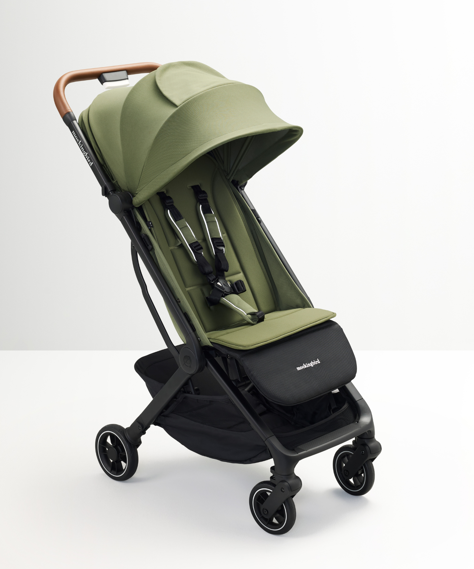 The Mockingbird Travel Stroller – Coming Soon! by Mockingbird is a green, feature-rich stroller with a canopy, black frame, brown handlebar, and four wheels, displayed on a white surface against a plain white background.