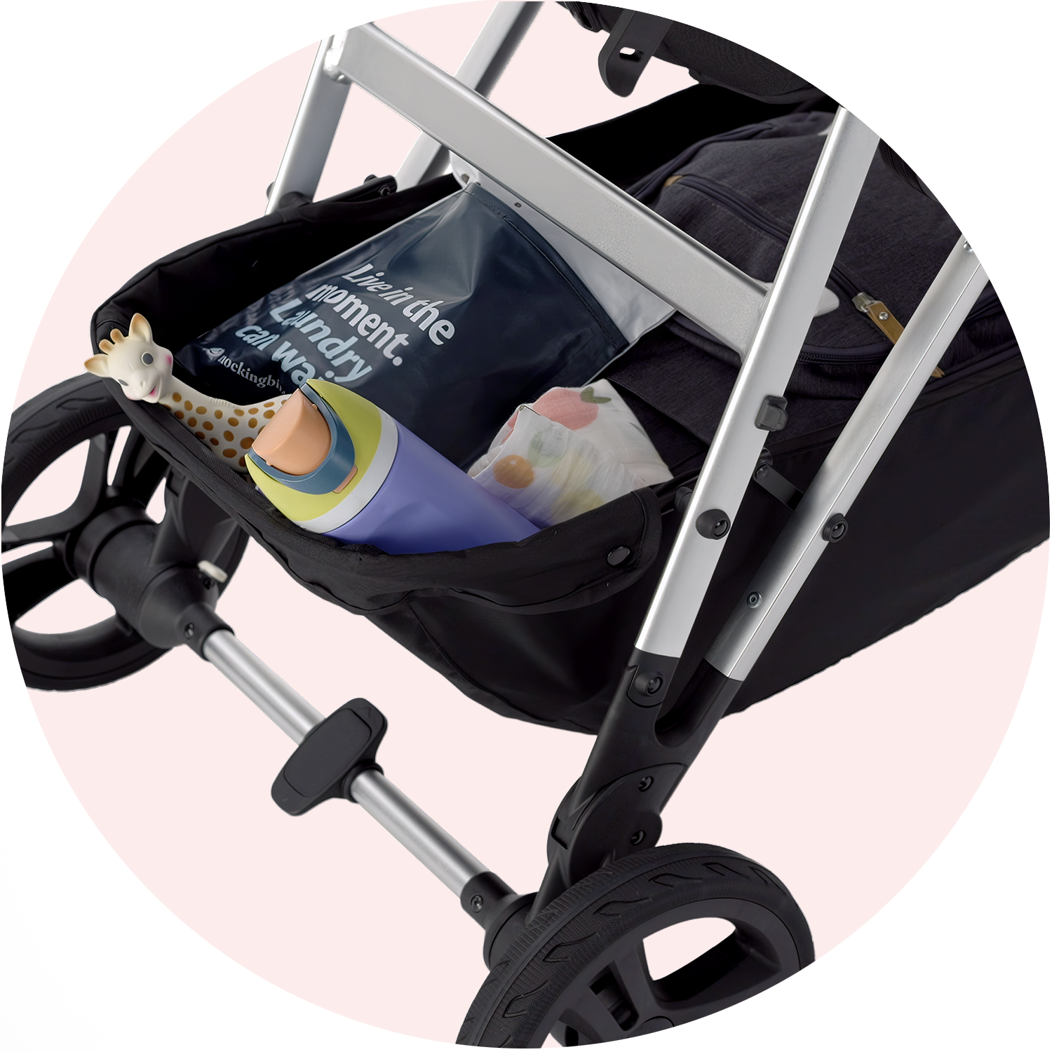 Underneath of a baby stroller showing a storage compartment filled with a baby bottle, a stuffed giraffe toy, and a bag of baby wipes.