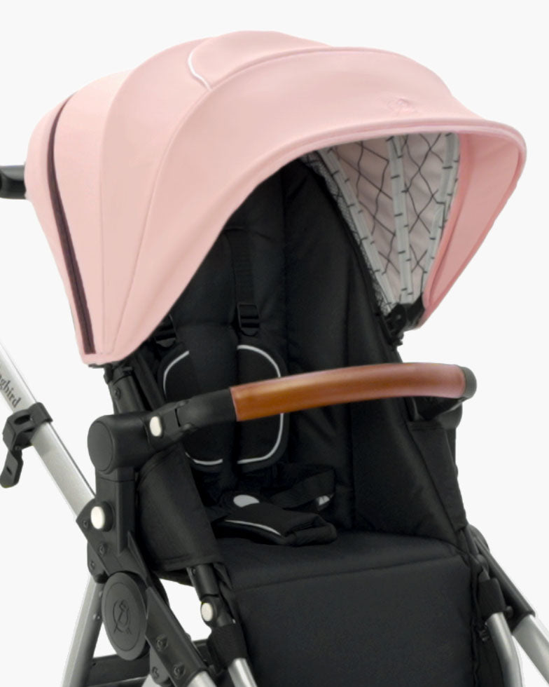 Close-up of a modern mockingbird-prod Extra Stroller Canopy 2.0 featuring a pink canopy, black seat, and a brown handle. #color_bloom