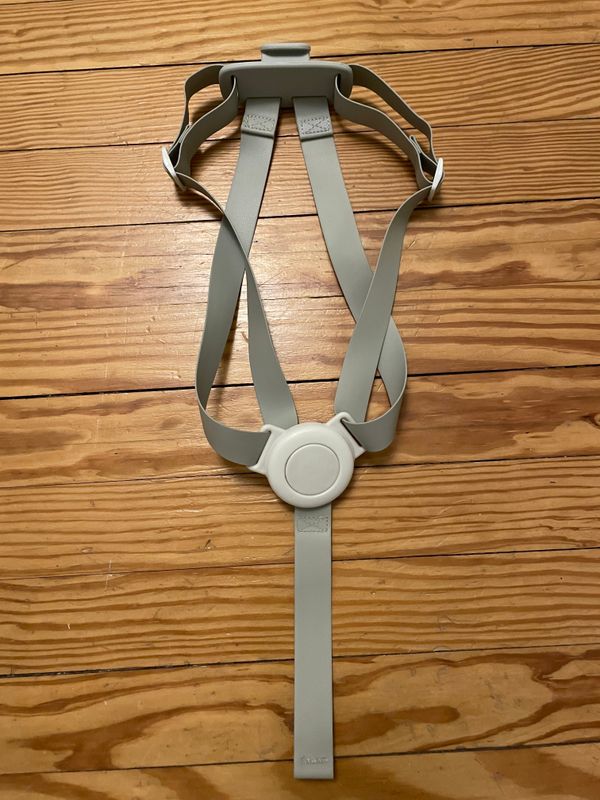 A grey adjustable strap device with a circular component in the middle and sturdy shoulder straps, the Mockingbird Harness (Copy), is laid out on a wooden floor.