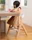 little girl sitting in child mode of the mockingbird high chair eating an apple and reading