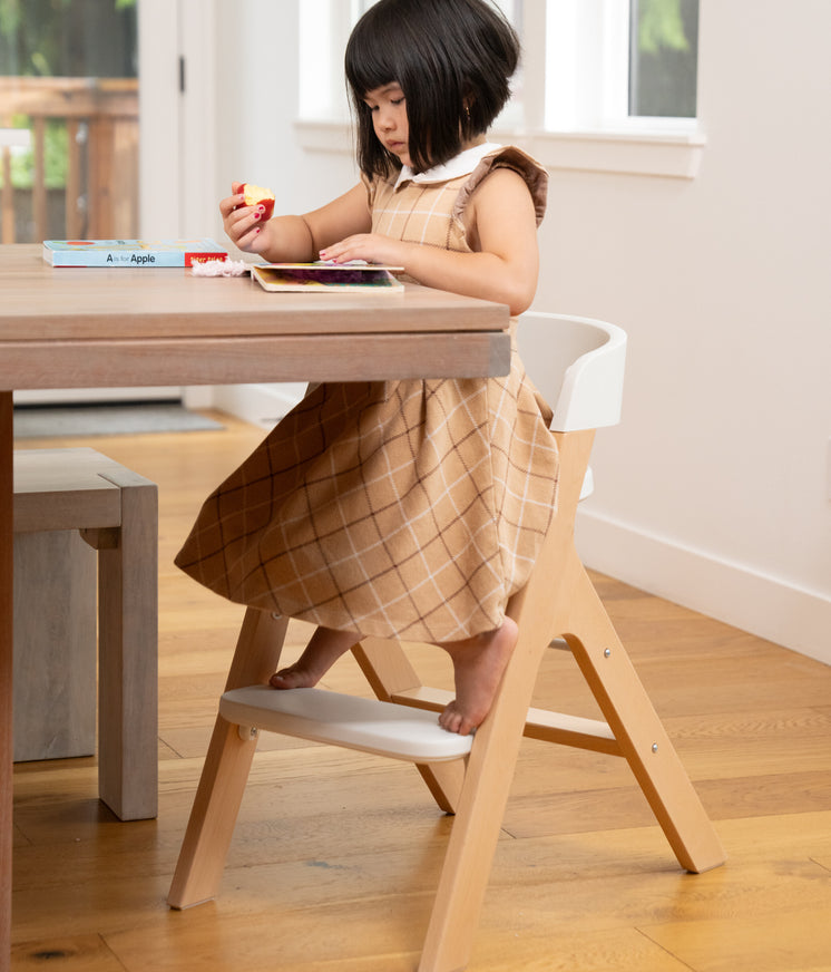 little girl sitting in child mode of the mockingbird high chair eating an apple and reading