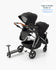 A modern single-to-double stroller with a second seat kit, featuring a sleek black design with a wooden handlebar and a small attached riding board.