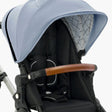 A modern mockingbird stroller featuring an Extra Stroller Canopy 2.0 in blue, a wooden handle, and a black fabric seat with safety harness. #color_sky