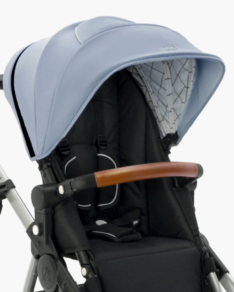 A modern mockingbird stroller featuring an Extra Stroller Canopy 2.0 in blue, a wooden handle, and a black fabric seat with safety harness. #color_sky