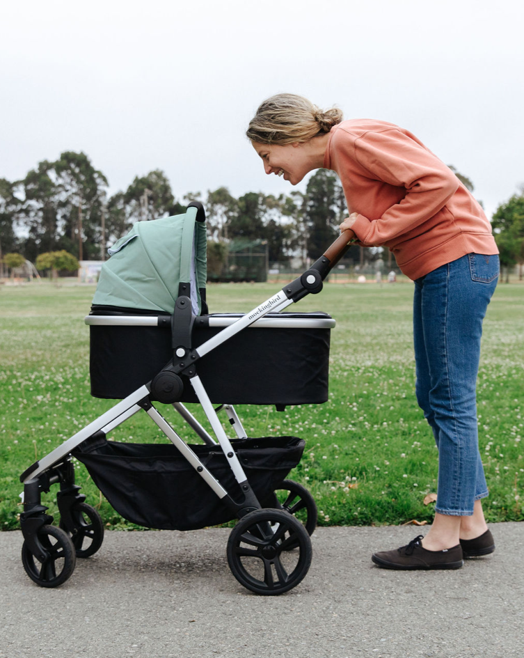 mom looking into her mockingbird stroller bassinet with sage green canopy